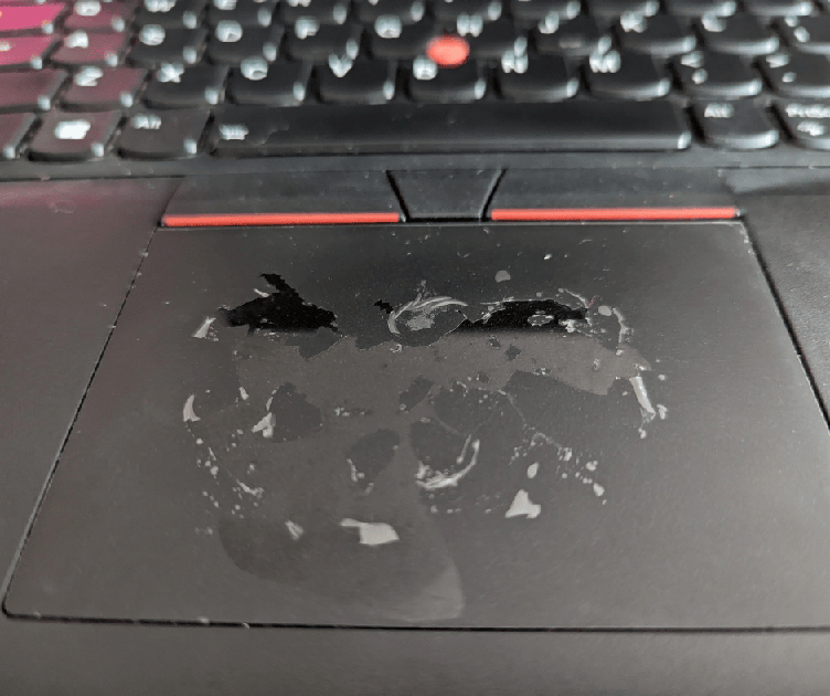 Close-up of a laptop touchpad with worn, smeared coating and circular wear marks, with a keyboard visible above.