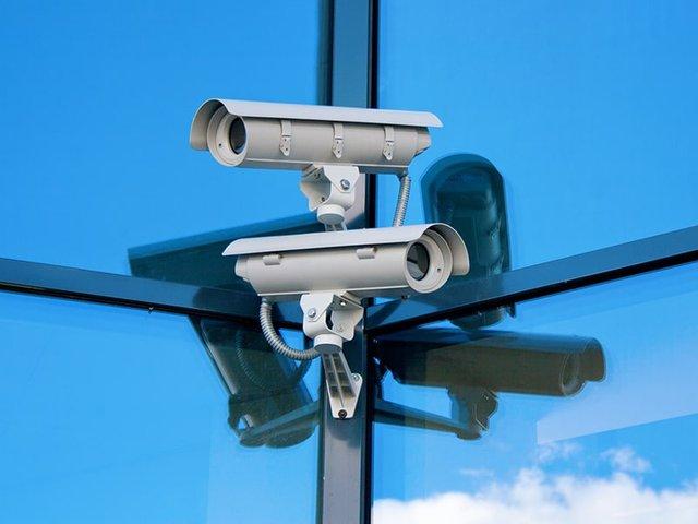 Two white surveillance cameras mounted on a glass storefront corner, overlooking the exterior area for security monitoring.